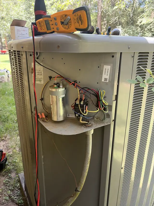 Technician testing a capacitor and contactor at an outdoor unit
